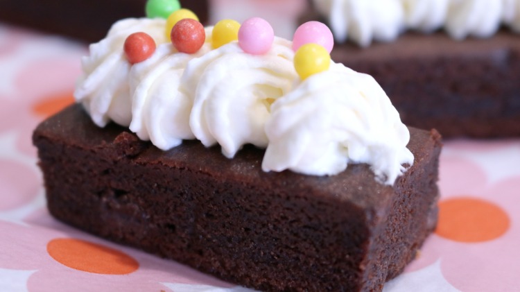 finger food brownie täckt med vispad grädde och dekorerad med sockerpärlor eller strössel