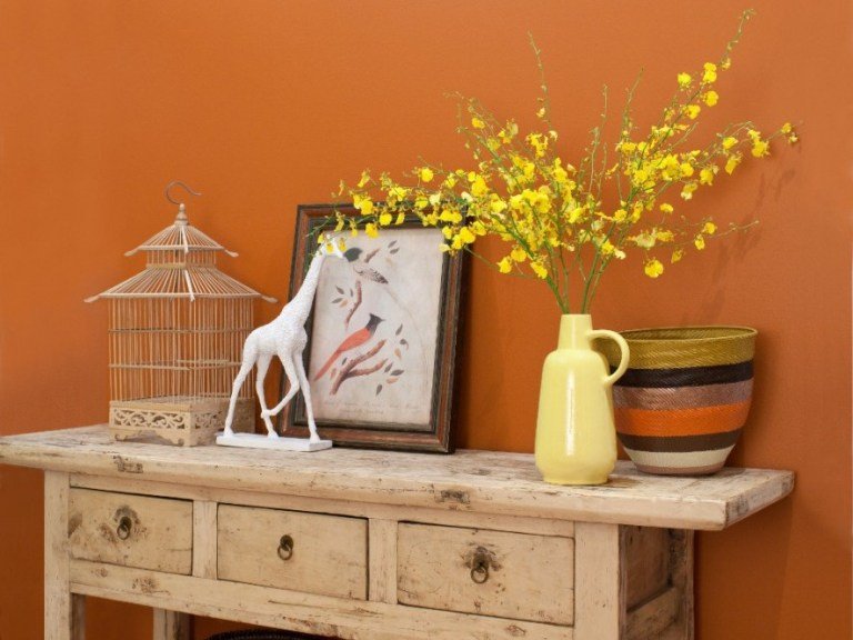 Orange vägg och vintage shabby chic inredning, gul porslin vas och fågelbur och rottingkorg som dekoration