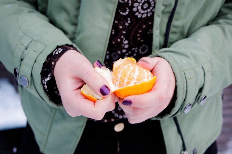 kvinna med lila manikyr skalar en mandarin utomhus i kallt väder