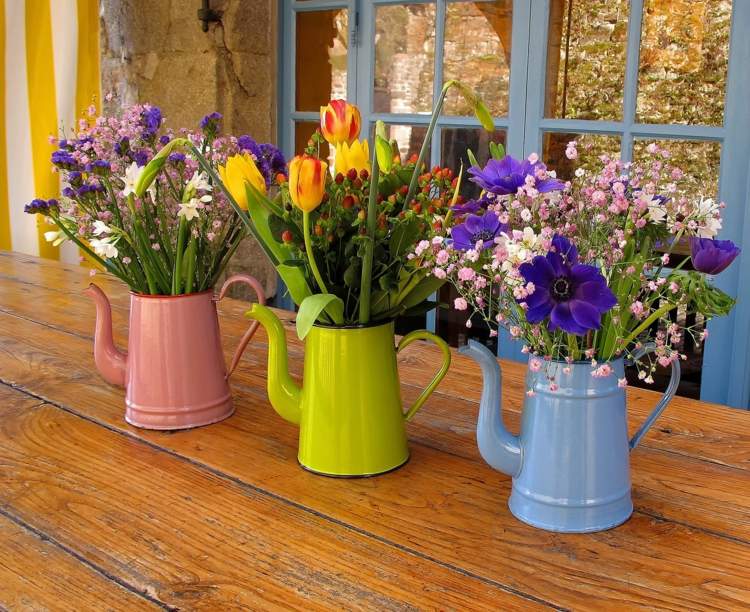 Vårblommor som buketter i färgglada metallkannor istället för vaser