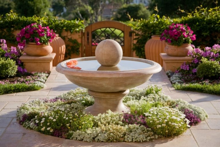 Trädgårdsfontän i sten i klassisk stil med blomsterbädd