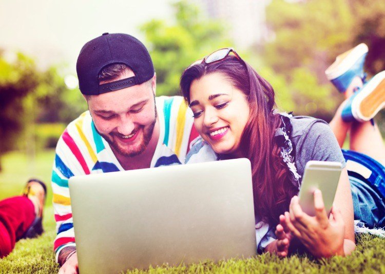 lyckligt par med bärbar dator och mobiltelefon som ligger på gräset i naturen