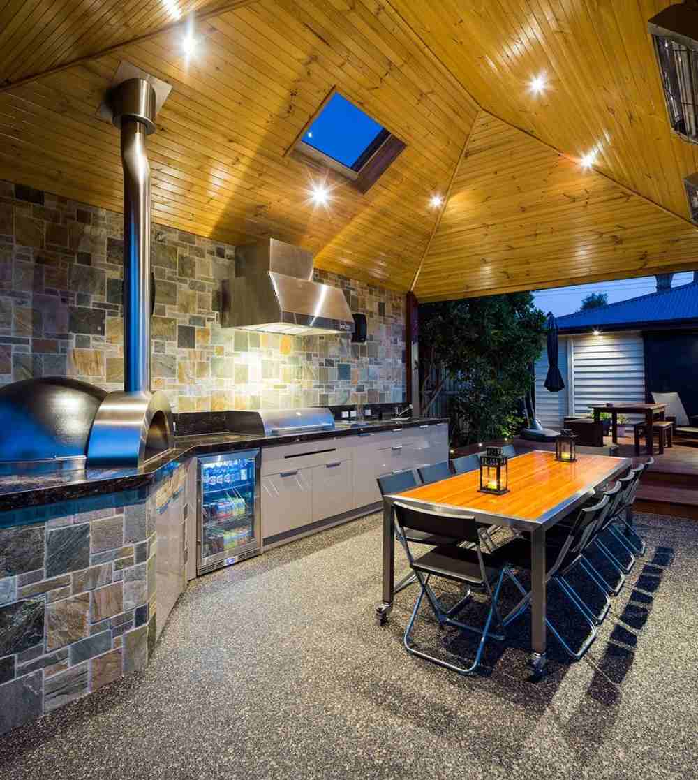 täckt utomhuskök med takfönster, inbyggt kylskåp och matbord samt pizzaugn