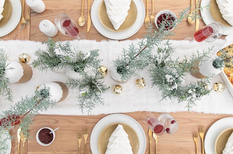 festlig bordsdekoration med vintergröna trädgrenar och gyllene keramiska vaser och bestick av guld och en servett vikt som en julgran