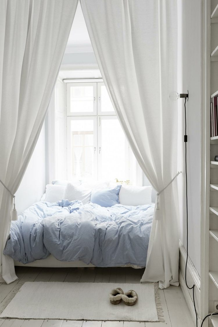 Säng i en fönsteralkov i ett vitt sovrum