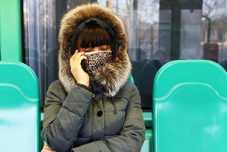 Kvinnan bär tygmask och väntar vid busshållplatsen