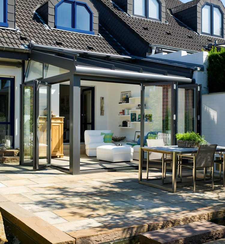 Fällbara glasdörrar-vinterträdgård-hus-förlängning-vardagsrum-vit-inredning-terrassplattor-natursten