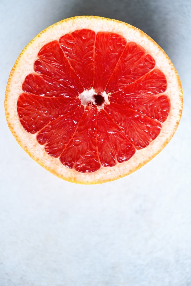 Citrusfrukter halverade med röd fruktkött på en grå bakgrund