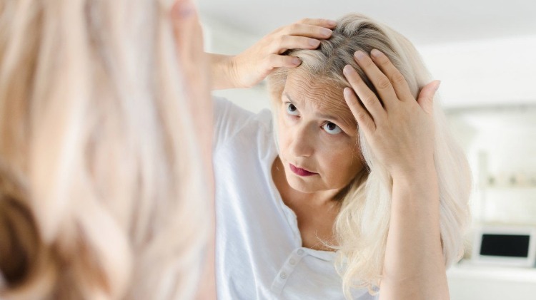 kvinna tittar på sitt gråa hår i spegeln