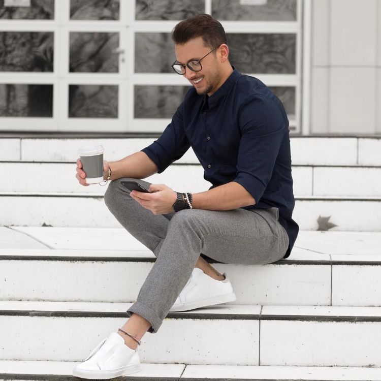 vita sneakers blå skjorta glasögon kaffe trappor mobiltelefon leende