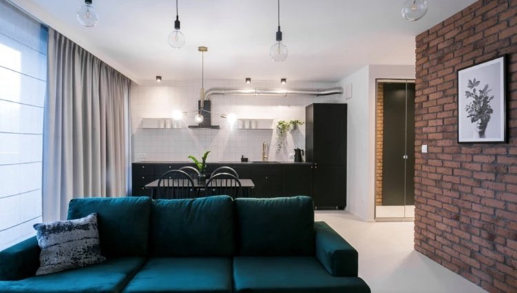 bensingrön soffa med ljusgrå gardiner och ett svartvitt kök kombinerat
