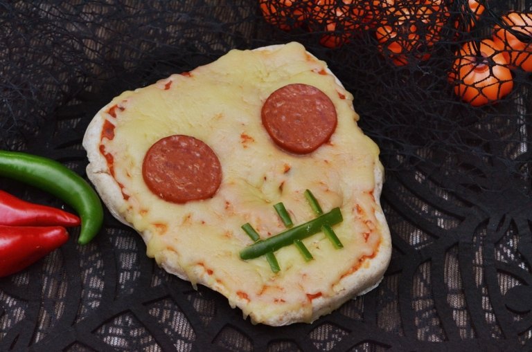 Rolig Halloween -pizza i form av en skalle med salami, paprika och ost