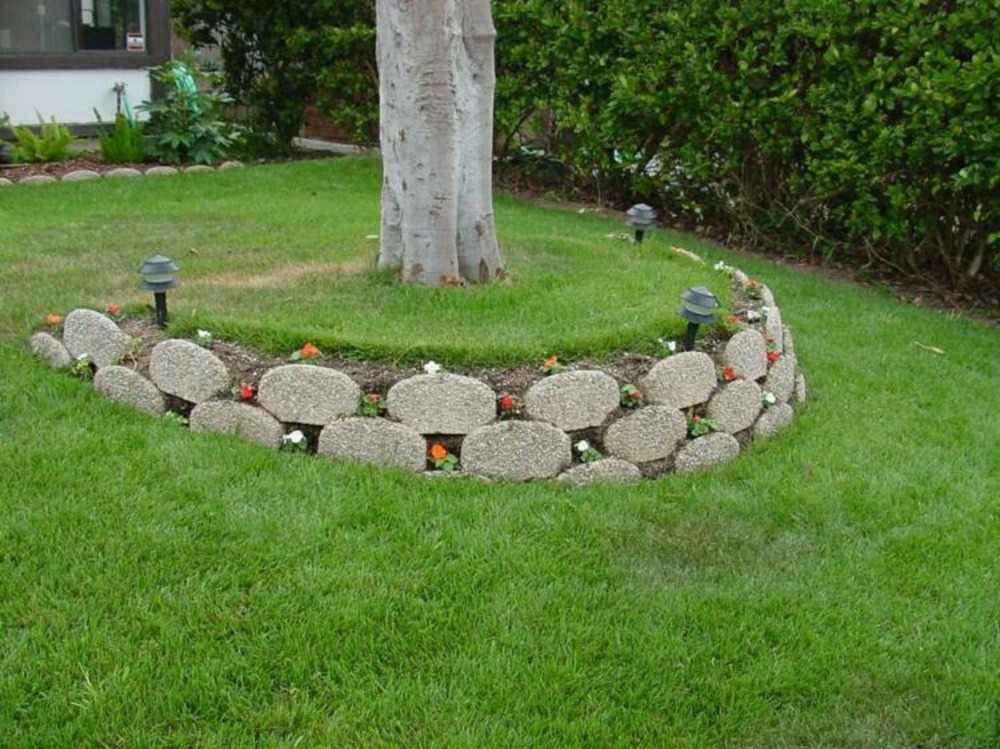 kombination av betongblock som en stödmur runt ett träd och gräsmatta med blommor i trädgården