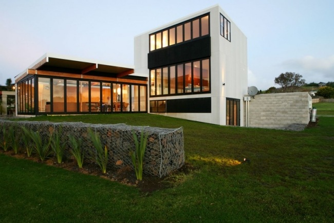Modernt hus vid kusten Nya Zeeland gräsmatta gabion tak-till-tak-inglasning