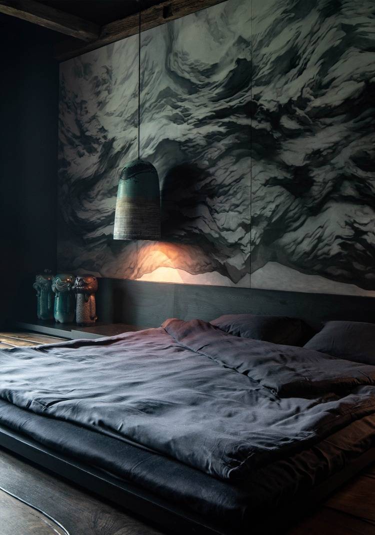 sovrum med sänggavel i mörkgrå toner och en pittoresk vägg av lera som en klippa