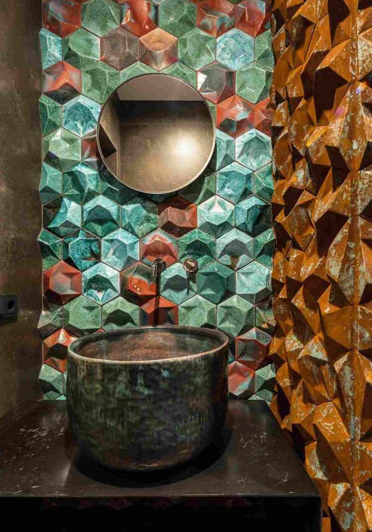 konstnärligt utformade väggar i ett litet badrum med handfat i koppar och en rund spegel