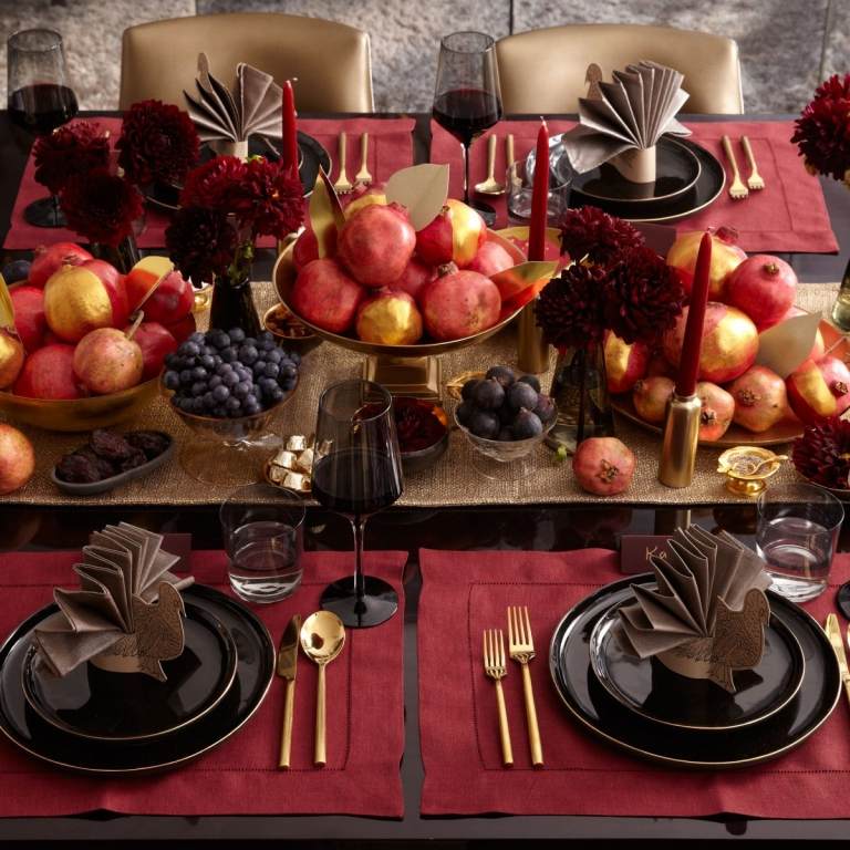 Höstens bordsdekoration med vinröda dahlior och frukter och druvor målade i guld och snyggt vikta servetter
