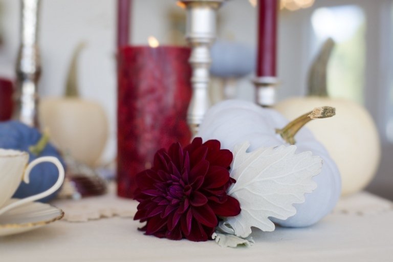 Höstbordsdekoration med dahlior i vit-röd-vita färgade höstlöv och dekorativa pumpor på bordet