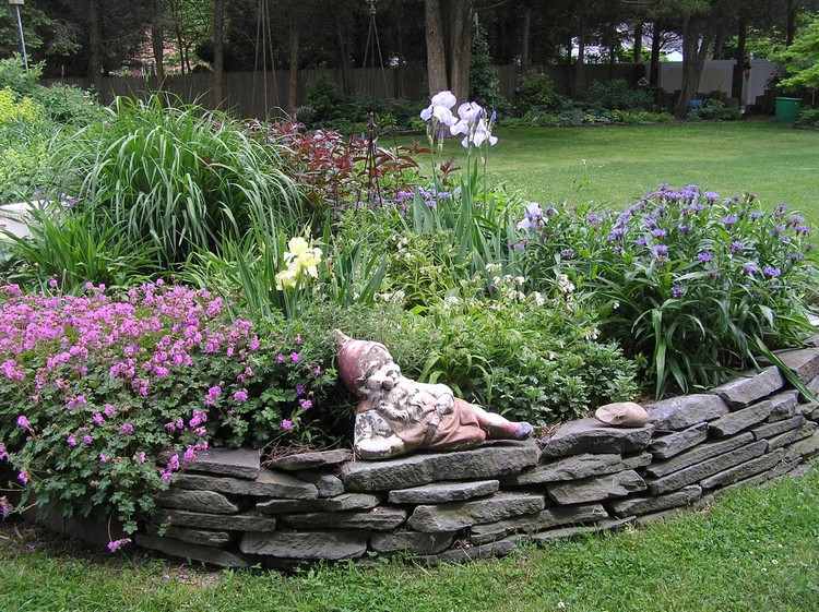 upphöjd-säng-gjord av sten-trädgård-tomtar-grå-tegel-blommor-växter-bakgård-grön-äng