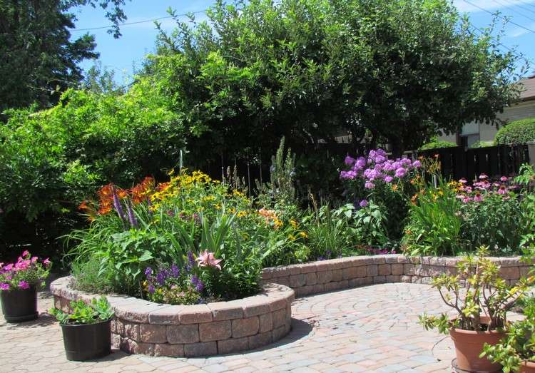 upphöjd-säng-gjord-av-sten-vägg-sten-plantering-färgglada-blommor-trädgård-grön-sommar