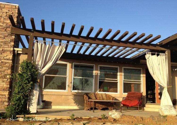 trä-pergola-gardiner-natursten-vägg-trä-konstruktion-mörk-soffa-fåtölj-järn-rotting