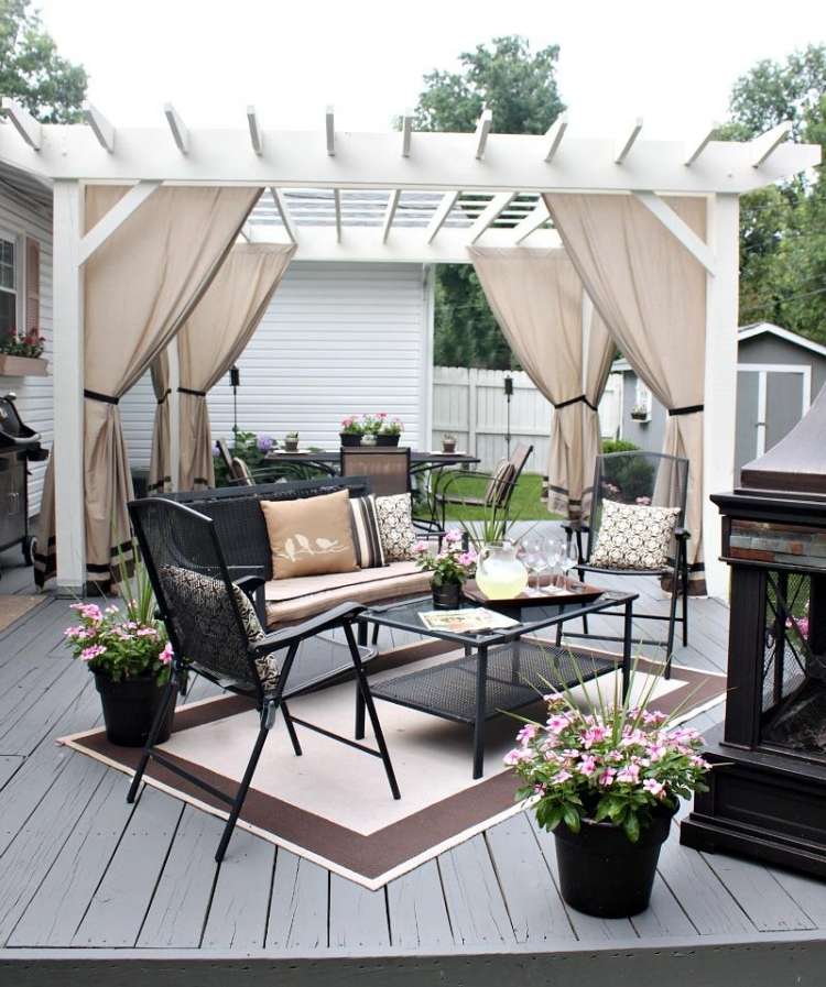 trä-pergola-gardiner-vit-svart-planka-golv-trädgårdsmöbler-metall-kuddar-beige-planter-matta