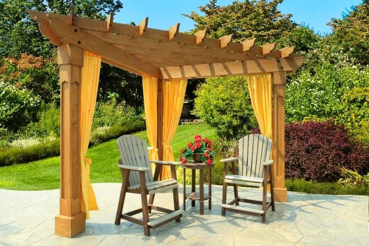 trä-pergola-gardiner-triangulära-gula-tyg-trästolar-gräsmatta-buskar