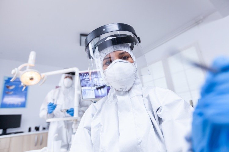 Kvinnlig tandläkare bär skyddsvisir under behandling av patienten på grund av covid 19 -pandemin