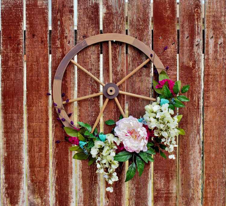 Dekorera trävagnshjulet med konstgjorda blommor och häng upp det på trädgårdsstaketet