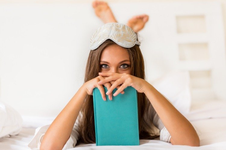 ung kvinna i sängen med sovmask och bok