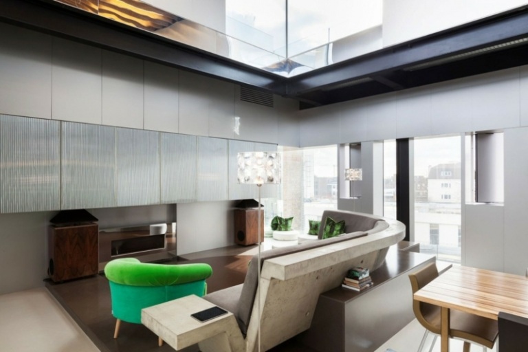 interiör av betong och aluminiumgrå soffa grön fåtölj förvaringsvägg ljusgrå träskåp