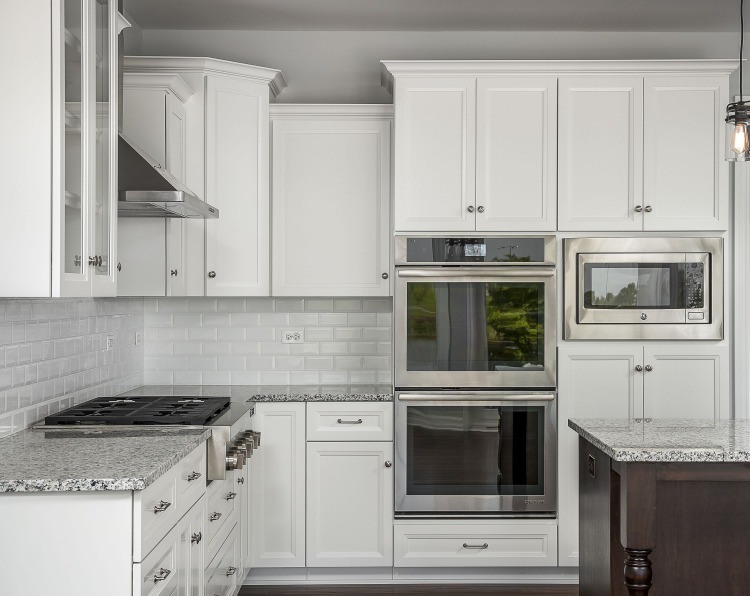 ädelt kök med vita väggskåp och mikrovågsugn i kombination med två ugnar och kokplattor