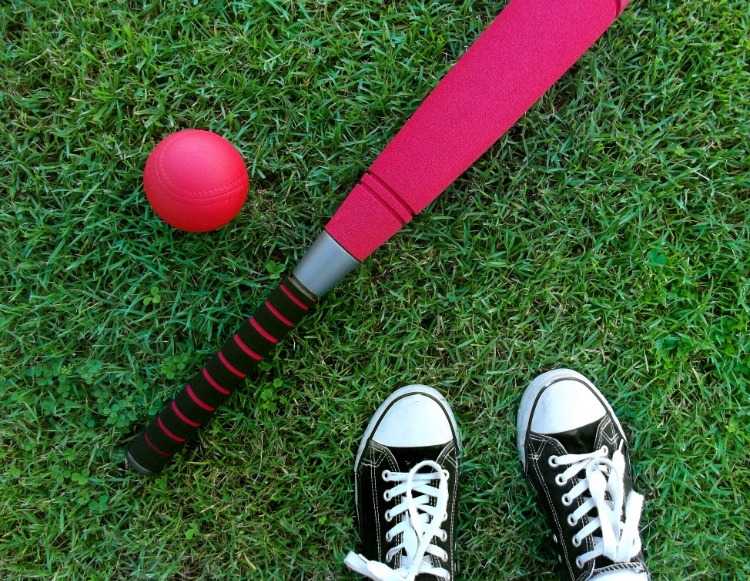 rosa basebollträ och boll bredvid sneakers på grönt gräs