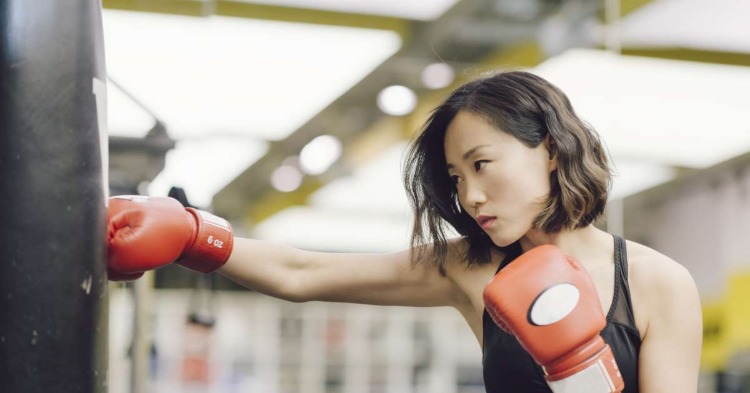 Asiatisk kvinna som slår slagpåse med boxhandskar i ett sportrum