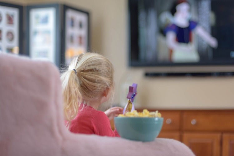 liten flicka som tittar på tv med popcorn hemma