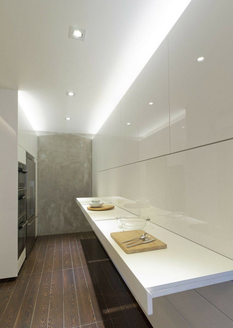 Inred en liten lägenhet kök-inbyggt skåp-utdragbar bänkskiva-vit-högglansat trägolv