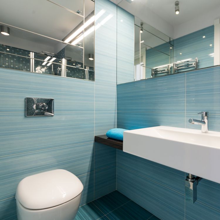 litet badrum med ljusblå kakel många speglar reflekterar ljuset och får rummet att se större ut
