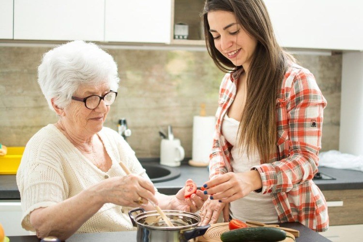 ung kvinna hjälper den gamla damen med alzheimer att känna igen ingredienserna i matlagningen