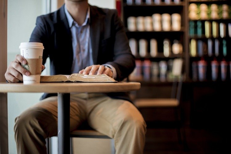 man sitter på café med böcker i bakgrunden och läser bok