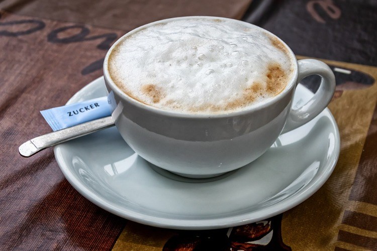 cappuccino med skum i vit kopp med fat och socker