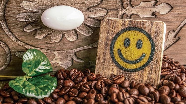 Kaffebönor och smiley med gröna blad framför en rustik låda