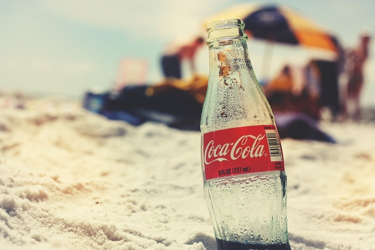tom coca cola -flaska i sanden på stranden