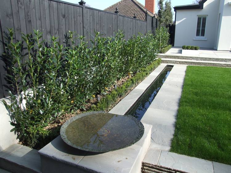 konstgräs-trädgård-terrass-vatten-funktion-vattenkälla-buskar-sekretess-skärm-trä