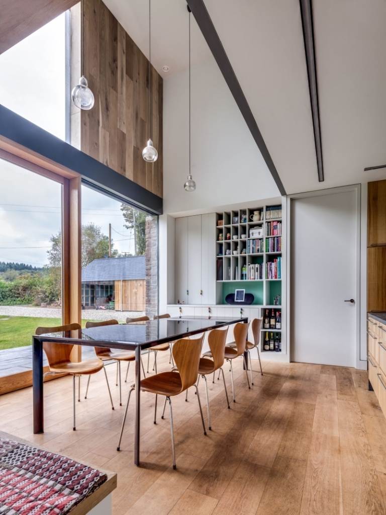 Lantligt hus -moderna-arkitektur-inredning-matplats-trägolv-matbord-stolar-högt i tak-vita-hängande-lampor-hylla-väggstöd