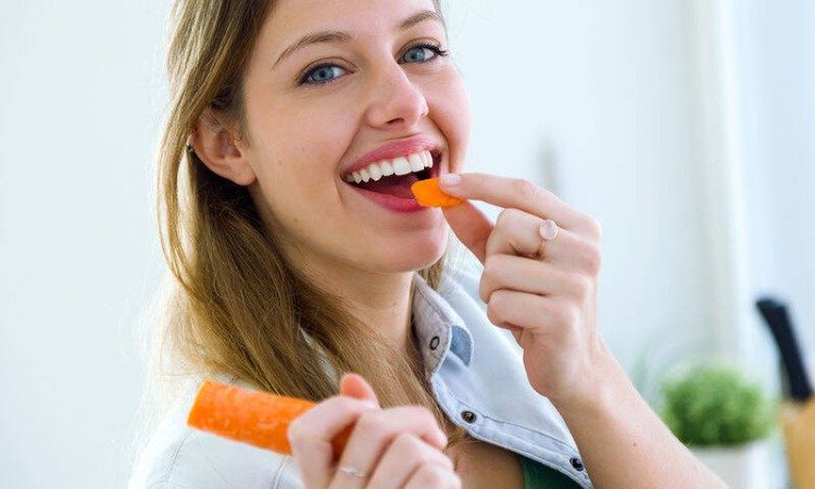ung kvinna äter morot för friska tänder och vackert leende