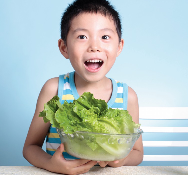 Litet barn håller skål med bladgrönsaker i form av blad från sallad