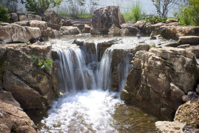 Vitt brusskapande vattenfall med stenformad trädgård