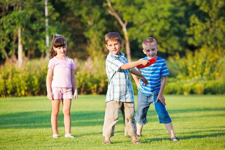 Barnlekar i trädgården som kastar röd-frisbee-vänner-sommardag