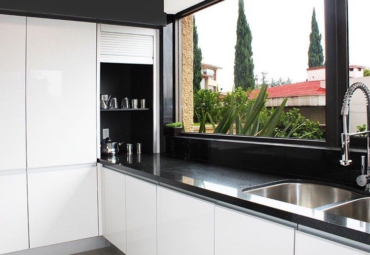 vitt kök med svart bänkskiva och handfat framför fönstret