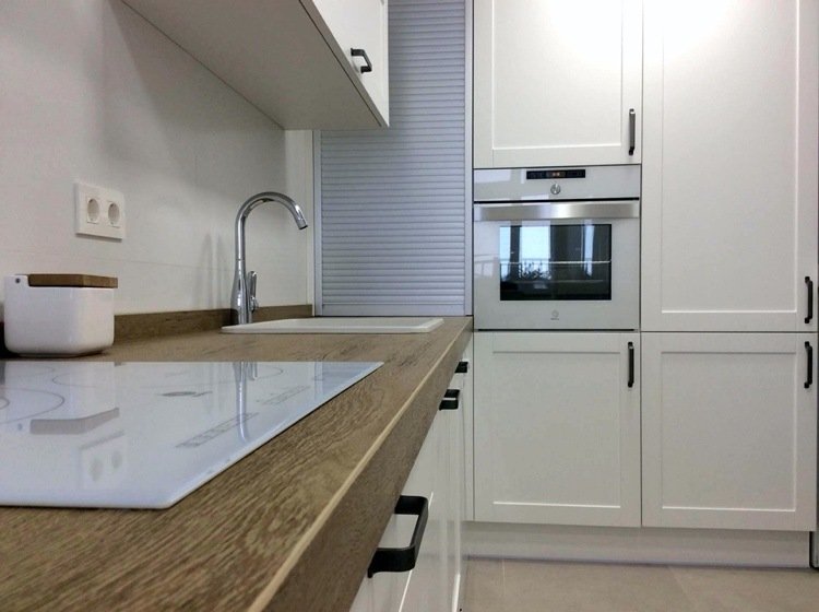 vitt kök med svarta handtag, bänkskiva i trä och rullskyddssystem i aluminium